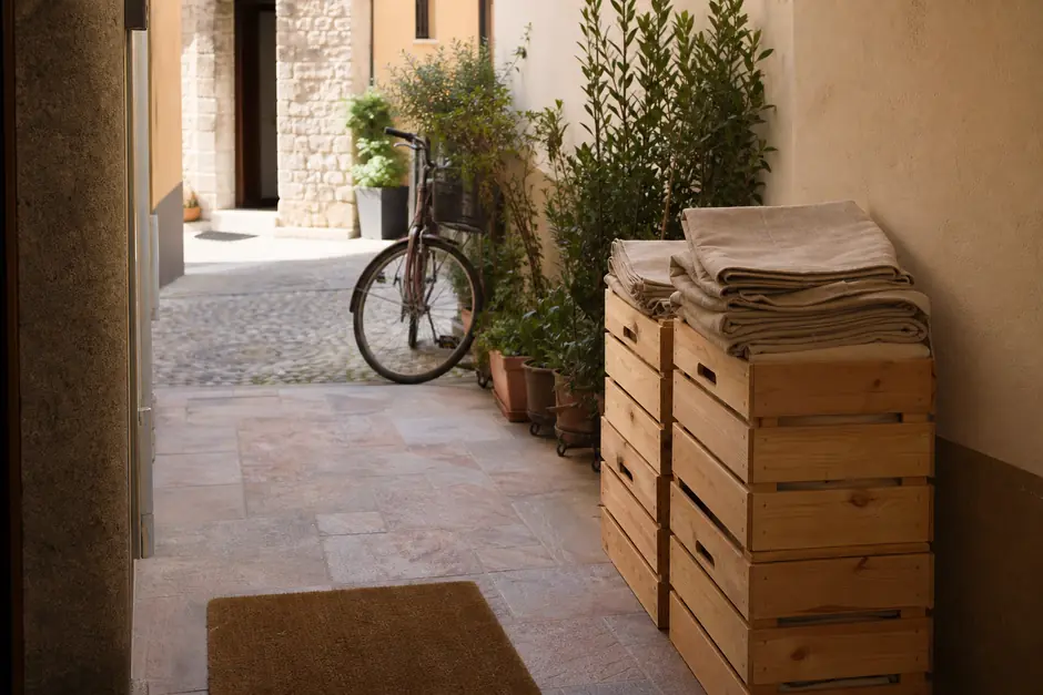 Ingresso nel giorno del ritiro: cassette impilate a coppie, borse di lino sopra, una bicicletta e uno zerbino (immagine generata con AI)