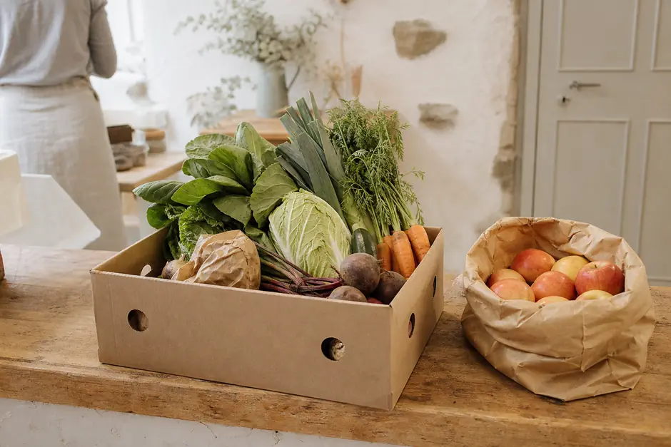 Cassetta di verdure miste preparata per il ritiro su un banco di legno, sacchetto di carta con mele accanto (immagine generata con AI)