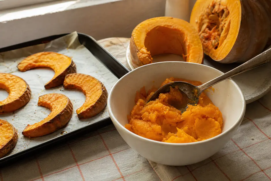 Fette di zucca arrostite su una teglia con carta da forno, un cucchiaio che raccoglie la polpa morbida in una ciotola (immagine generata con AI)