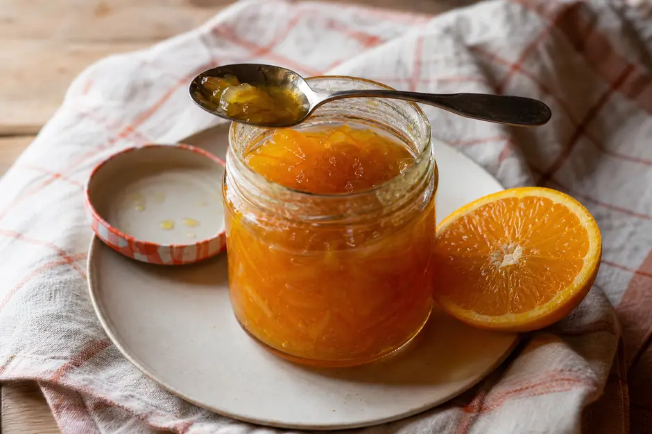 Barattolo aperto di marmellata di arance lucida con fette di agrume accanto (immagine generata con AI)