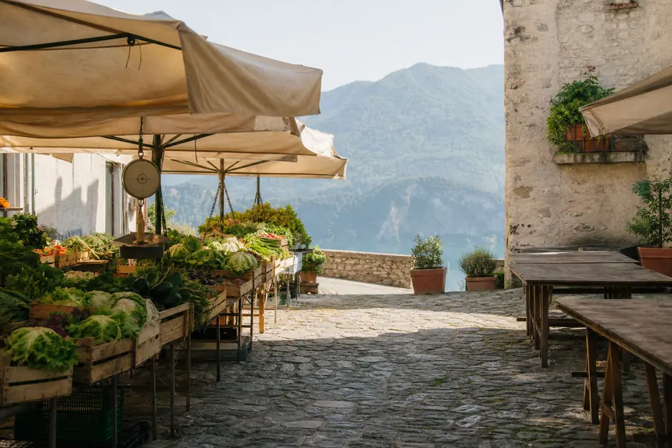 Mercato agricolo in una piazza di pietra con teloni di canapa e casse di verdura (immagine generata con AI)